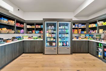 A refrigerator filled with drinks and snacks sits in the middle of a room with shelves stocked with various food items.